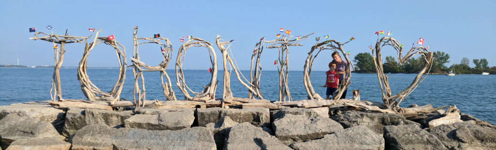 A stick sculpture spelling out Toronto on the shore of lake Ontario with a heart and flags of the world
